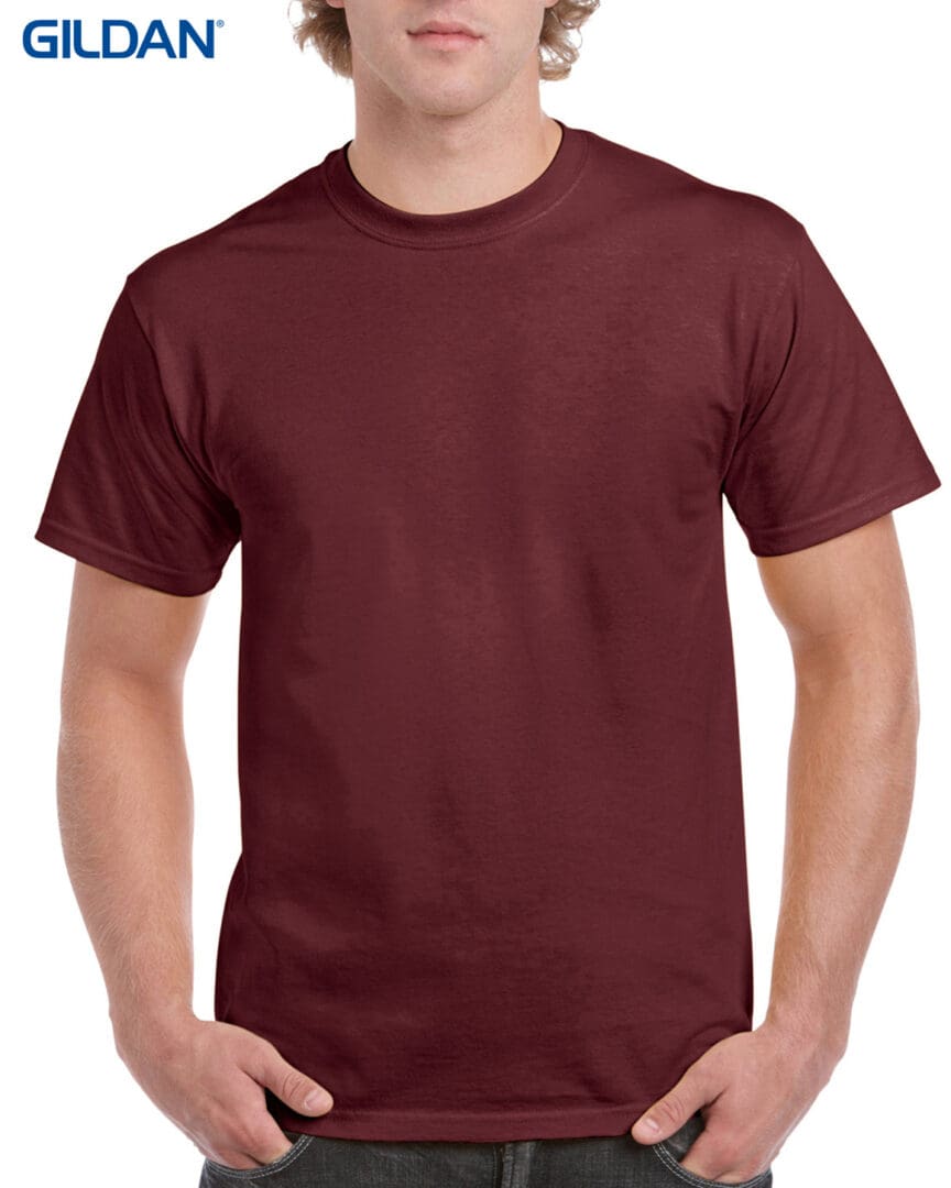 A man wearing a maroon t-shirt with his hands in his pockets.