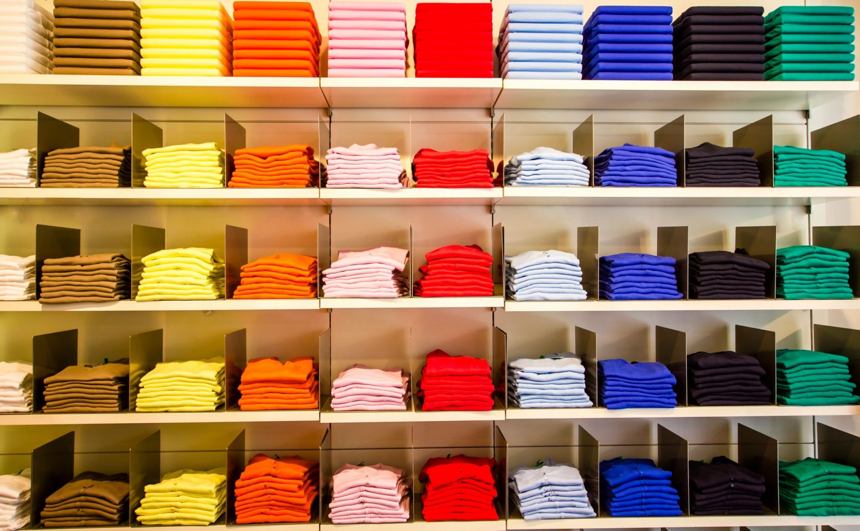 A shelf filled with many different colored shirts.